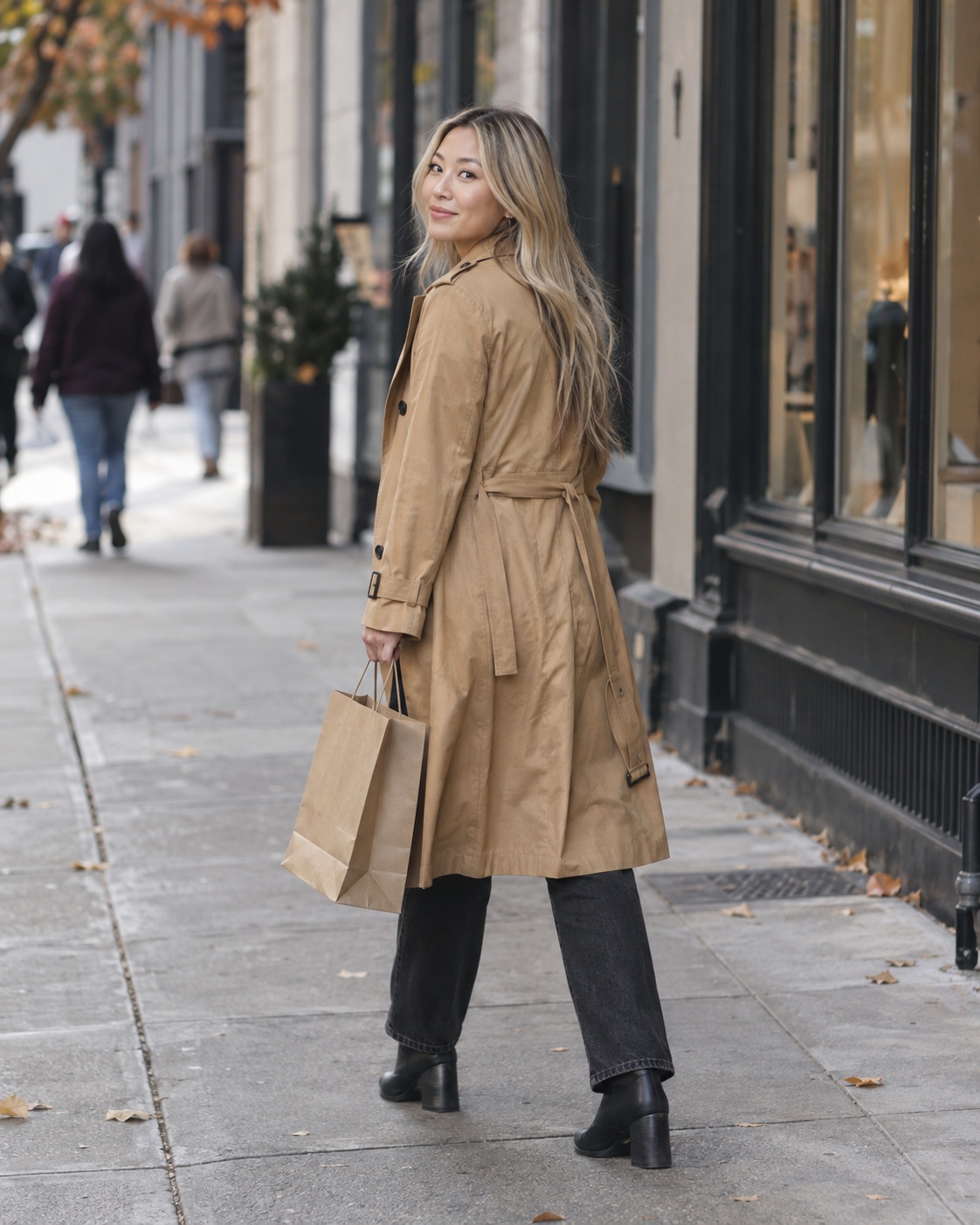 East Asian woman with long champagne-blonde hair walking past city storefronts with a shopping bag